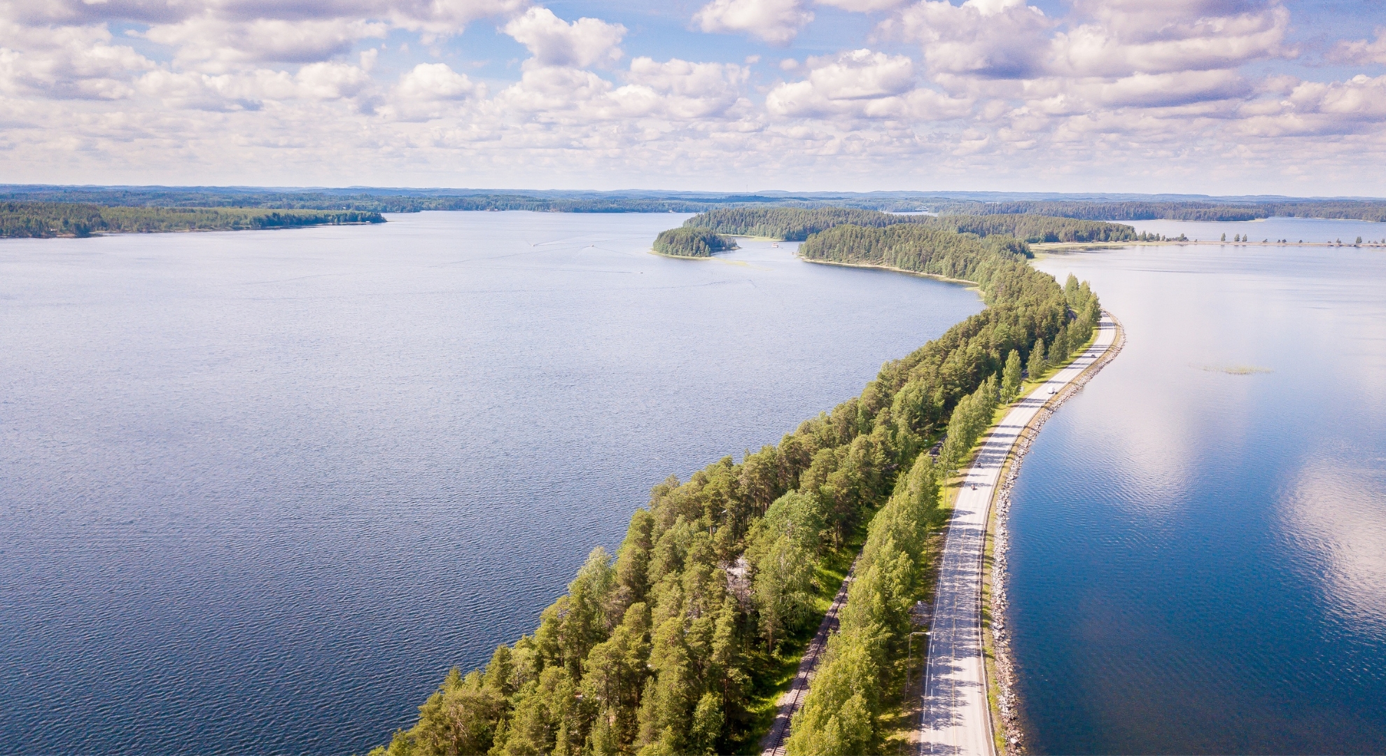 A lengthy road runs through calm waters, illustrating the picturesque landscape of Finland.