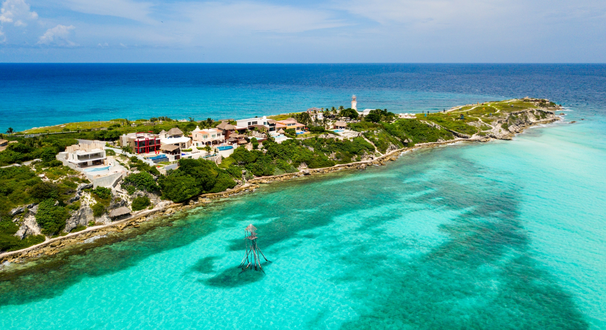 Aerial image of a small island in Mexico, highlighting a lighthouse against a backdrop of vibrant blue sea.