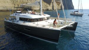 A catamaran, S/Y KASKAZI FOUR, is anchored peacefully in the water, showcasing its sleek design and luxury.