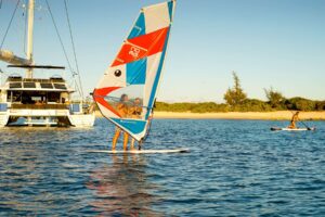 A man windsurfing on the water with the super yacht S/Y KASKAZI FOUR visible in the background.